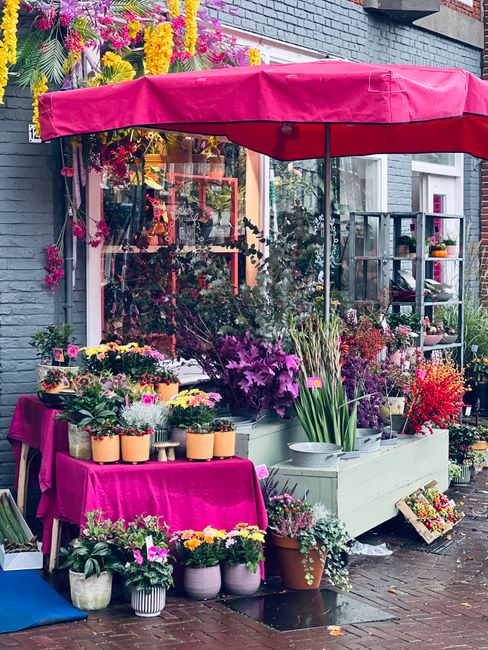 A vibrant floral display outside a flower shop on Ascot High Street, featuring an arrangement of fresh flowers including purple irises and pink chrysanthemums, placed on a white wooden stand under a l